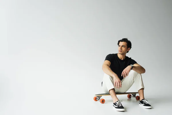 Young man in black t-shirt sitting on longboard on grey — Stock Photo
