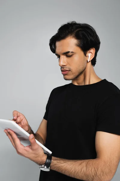 Молодий чоловік в навушниках за допомогою цифрового планшета ізольований на сірому — стокове фото