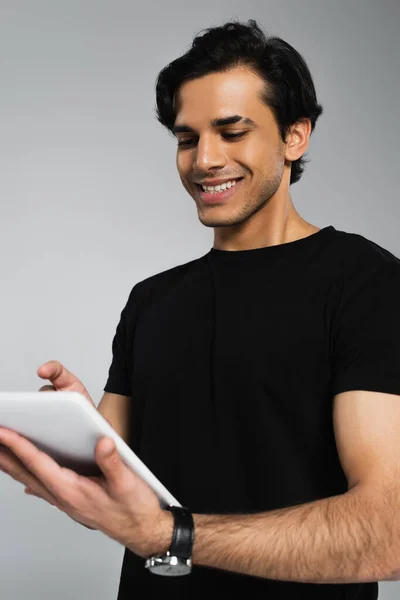 Joven feliz en camiseta negra usando tableta digital aislada en gris - foto de stock