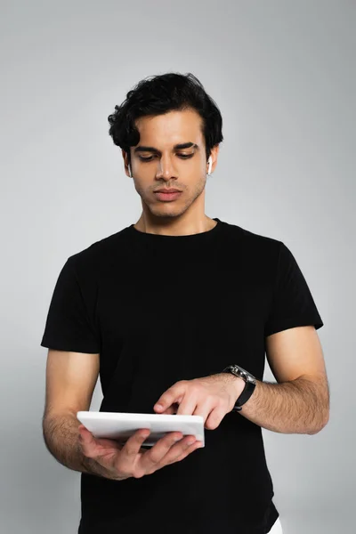 Молодой человек в черной футболке указывает на цифровой планшет, изолированный на сером — стоковое фото