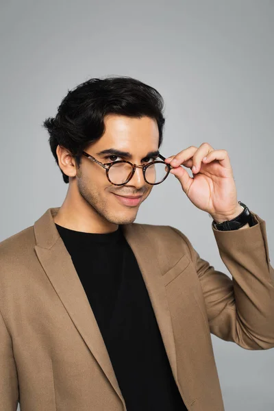 Pleased young man adjusting stylish eyeglasses isolated on grey — Stock Photo