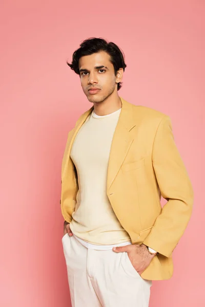 Joven en chaqueta amarilla posando con las manos en bolsillos en rosa - foto de stock