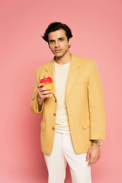Молодий чоловік в жовтому блістері тримає паперову чашку на рожевому — стокове фото