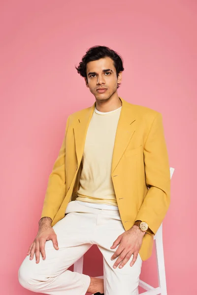 Jovem homem em blazer amarelo sentado na cadeira branca isolado em rosa — Fotografia de Stock