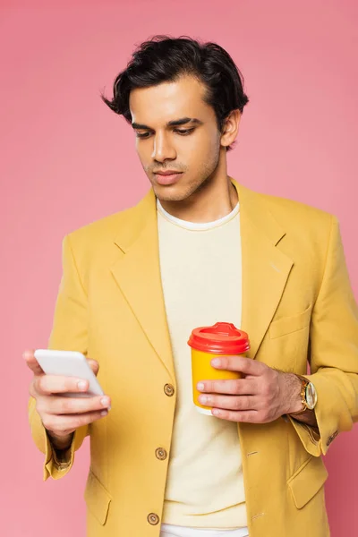 Junger Mann benutzt Smartphone und hält Pappbecher isoliert auf rosa — Stockfoto