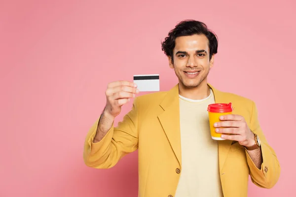 Jovem feliz segurando cartão de crédito e copo de papel em rosa — Fotografia de Stock
