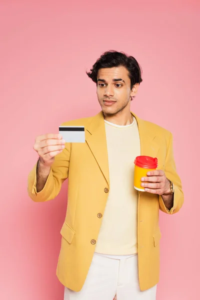 Jovem segurando cartão de crédito e copo de papel em rosa — Fotografia de Stock