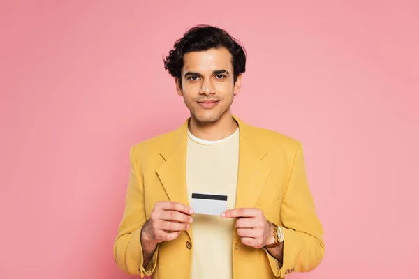 Homem sorridente em blazer amarelo segurando cartão de crédito isolado em rosa — Fotografia de Stock