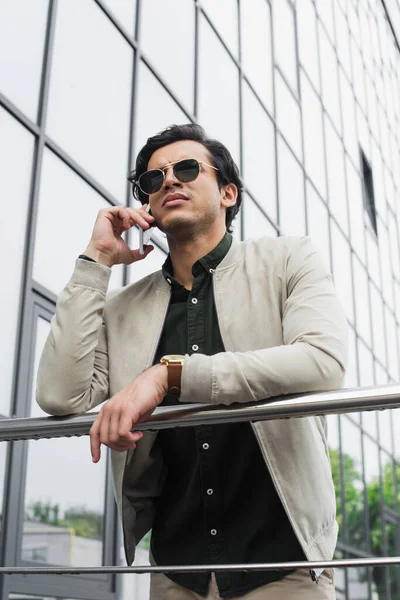 Vista de ángulo bajo de hombre joven con estilo en gafas de sol hablando en el teléfono móvil - foto de stock