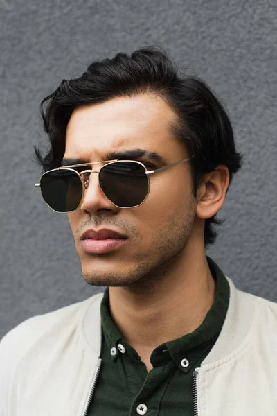 Portrait of young man in stylish sunglasses posing near grey wall — Stock Photo