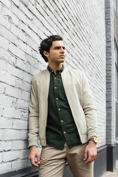 Young man in bomber jacket posing near brick wall — Stock Photo