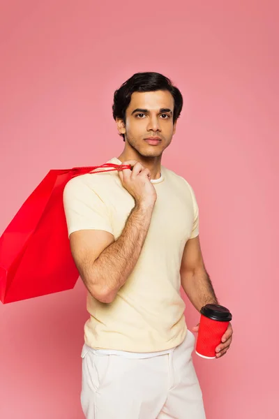 Young man holding paper cup and shopping bag isolated on pink — Stock Photo