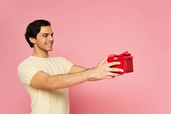 Jeune homme joyeux tenant boîte cadeau rouge isolé sur rose — Photo de stock