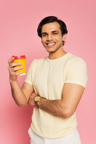 Joyeux jeune homme tenant tasse en papier avec café pour aller isolé sur rose — Photo de stock