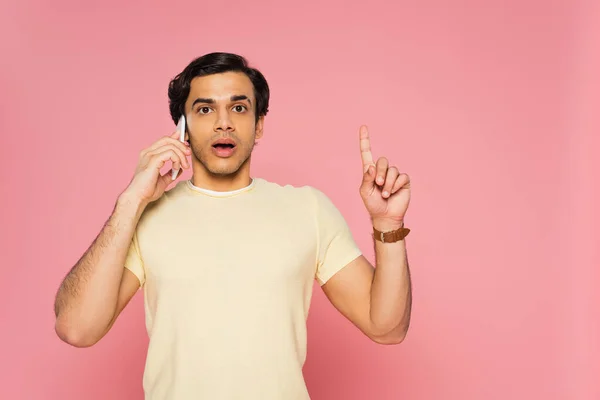 Sorprendido joven hablando en el teléfono inteligente, mientras que tener idea aislada en rosa - foto de stock