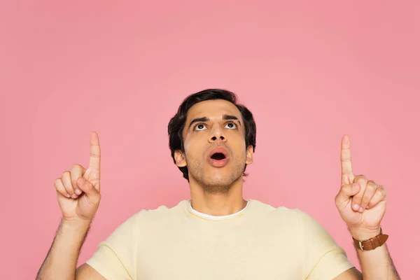 Impactado joven señalando con los dedos y mirando hacia arriba aislado en rosa - foto de stock