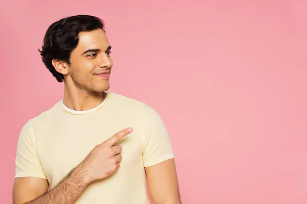 Joyful young man pointing with finger and looking away isolated on pink — Stock Photo