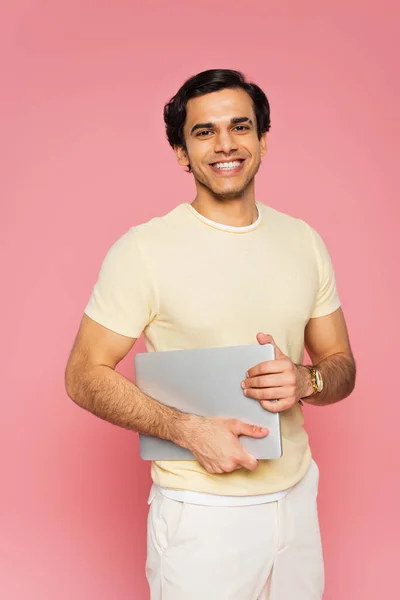 Alegre freelancer sosteniendo portátil aislado en rosa - foto de stock