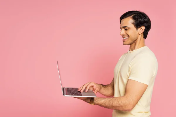 Alegre freelancer escribir en el ordenador portátil aislado en rosa - foto de stock