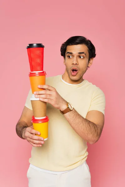 Sorprendido joven mirando vasos de papel apilados aislados en rosa - foto de stock