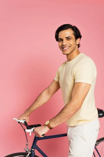 Jovem feliz de pé perto de bicicleta em rosa — Fotografia de Stock