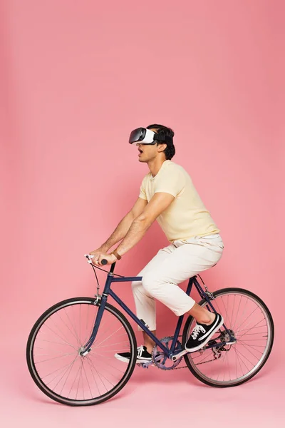 Hombre sorprendido en vr auriculares bicicleta de montar en rosa - foto de stock