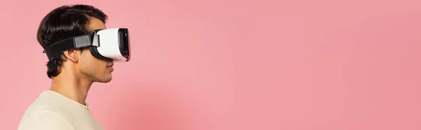 Вид збоку молодого чоловіка в гарнітурі vr ізольований на рожевому, банер — стокове фото