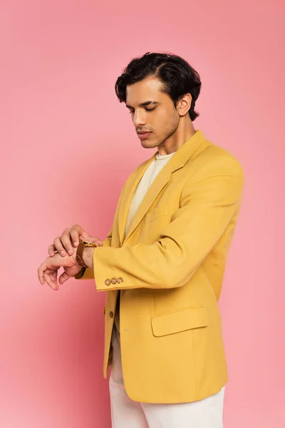 Elegante giovane uomo in giacca alla moda guardando orologio da polso su rosa — Foto stock