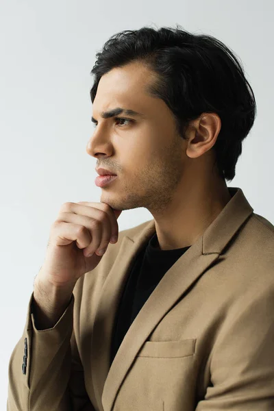 Pensativo joven en elegante chaqueta beige mirando hacia otro lado aislado en gris - foto de stock