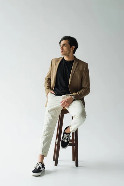 Young man in stylish beige blazer sitting on wooden chair on grey — Stock Photo