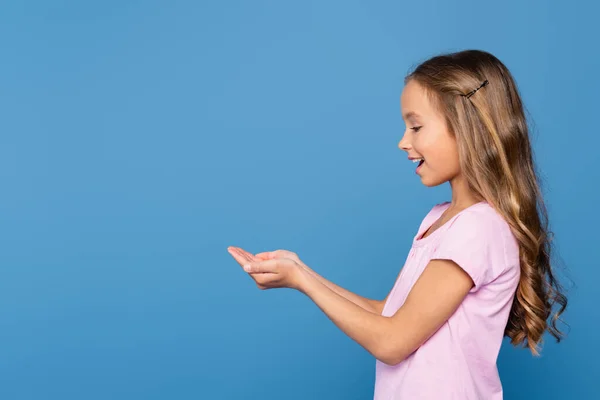 Vista lateral da menina sorridente com as mãos de chávena isoladas no azul — Fotografia de Stock