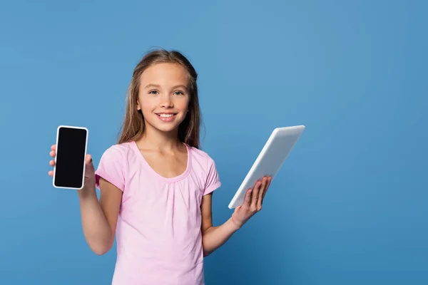 Kid segurando tablet digital e mostrando smartphone isolado em azul — Fotografia de Stock