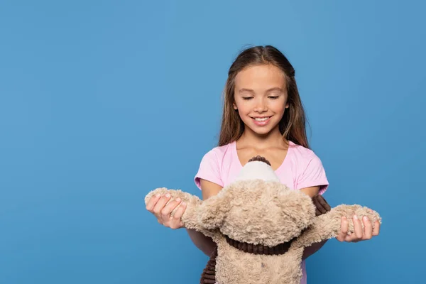 Positive kid looking at teddy bear isolated on blue — Stock Photo