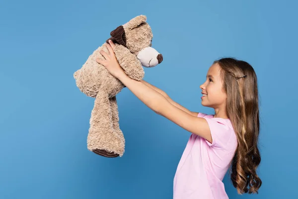 Side view of girl holding soft toy isolated on blue — Stock Photo