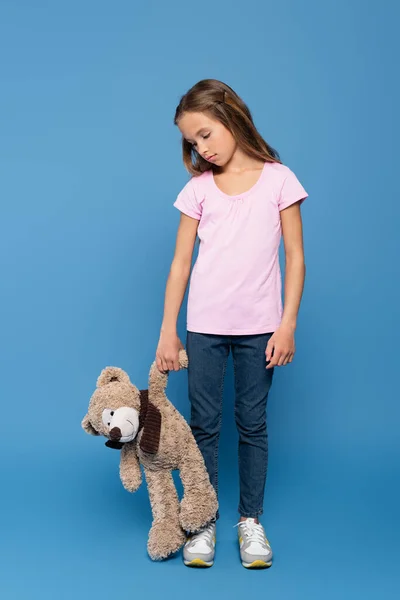 Sad girl holding teddy bear on blue background — Stock Photo