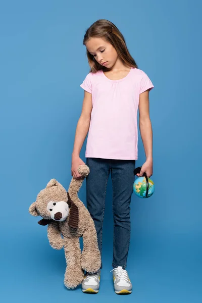 Triste garoto com globo olhando para ursinho de pelúcia no fundo azul — Fotografia de Stock