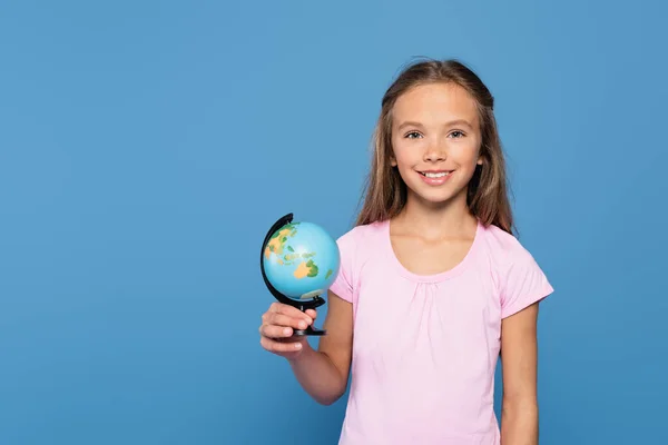 Lächelndes Kind mit Globus, das isoliert auf blauem Grund in die Kamera blickt — Stockfoto