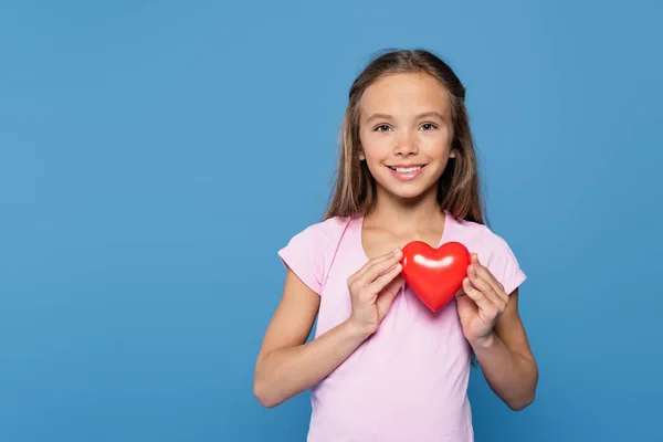 Menina com coração decorativo vermelho sorrindo para a câmera isolada em azul — Fotografia de Stock