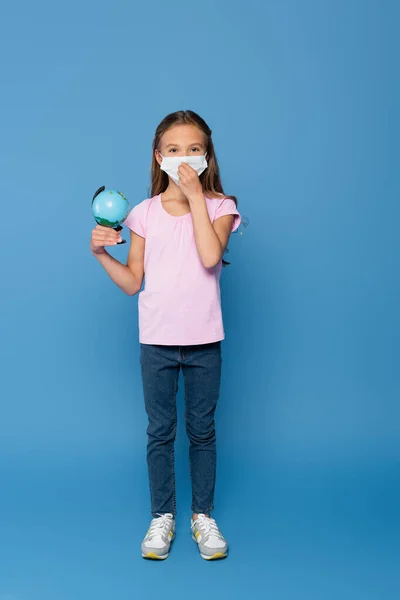 Girl wearing medical mask and holding globe blue background — Stock Photo