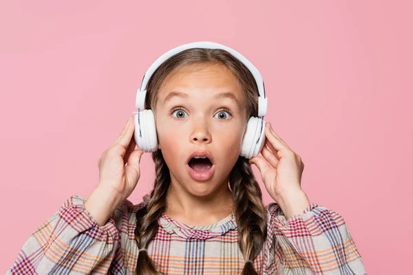 Amazed child in headphones looking at camera isolated on pink - foto de stock