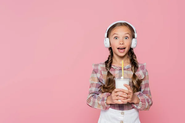 Criança excitada em fones de ouvido segurando milkshake isolado em rosa — Fotografia de Stock