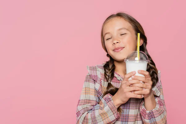 Pleased preteen girl with closed eyes holding milkshake isolated on pink - foto de stock