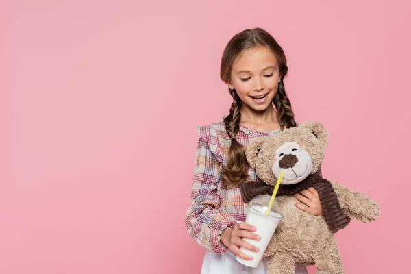 Kid in plaid shirt holding milkshake near teddy bear isolated on pink — Stock Photo
