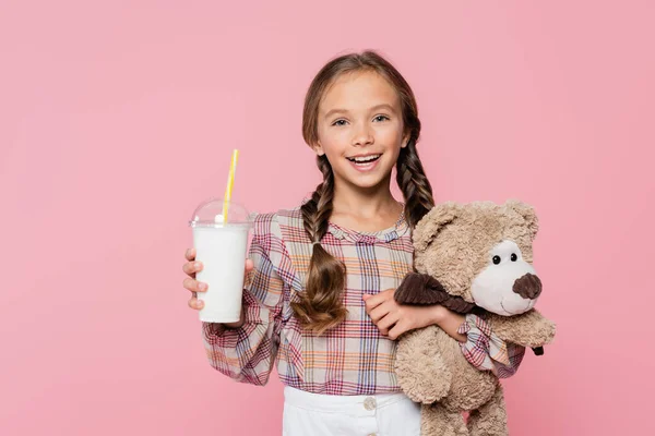 Happy preteen kid holding soft toy and milkshake isolated on pink — Photo de stock