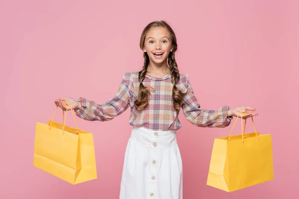 Positive kid holding yellow shopping bags isolated on pink — Photo de stock