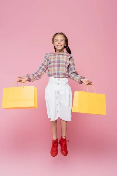 Criança pré-adolescente feliz com sacos de compras levitando isolado em rosa — Fotografia de Stock