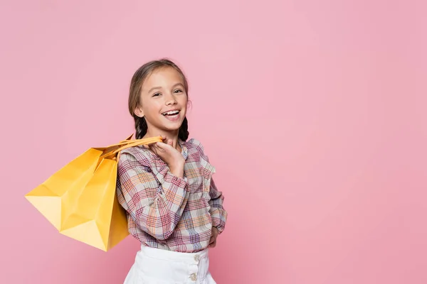 Menina alegre com sacos de compras amarelos sorrindo para a câmera isolada em rosa — Fotografia de Stock