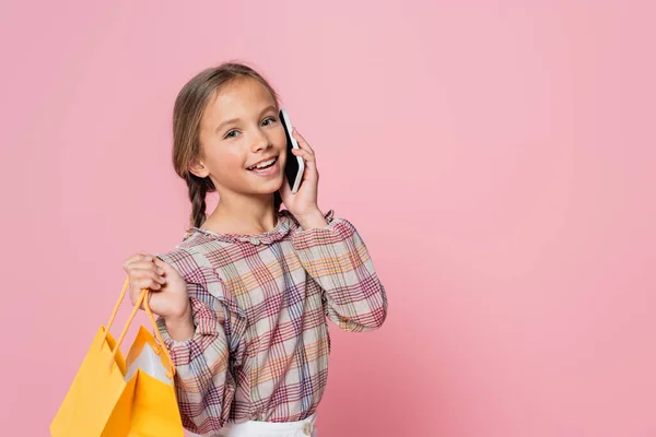 Preteen girl with yellow shopping bag talking on mobile phone isolated on pink - foto de stock
