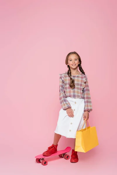 Stylish girl with yellow shopping bag near penny board on pink background — Stock Photo