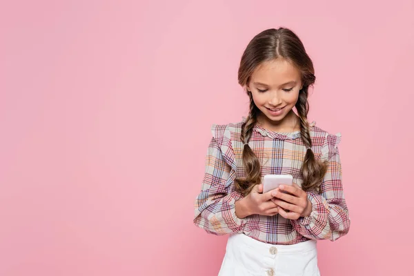 Усміхнена дівчина в картатій блузці обміну повідомленнями на смартфоні ізольована на рожевому — стокове фото